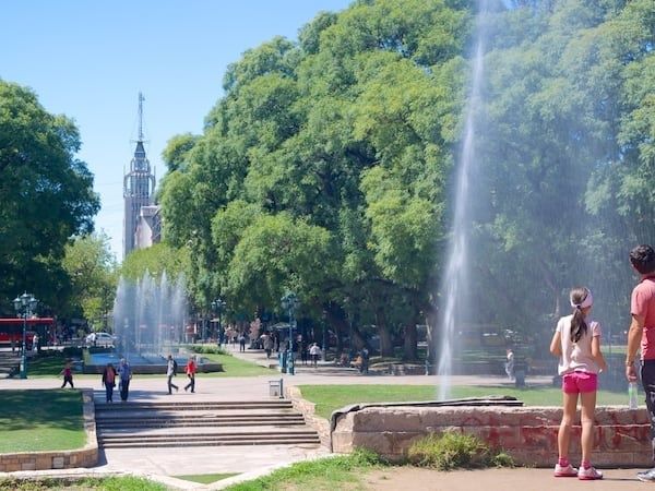 Visitors walk through a tree-lined square with fountains and steps