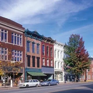 Historic downtown storefronts and parked cars along a tree-lined street